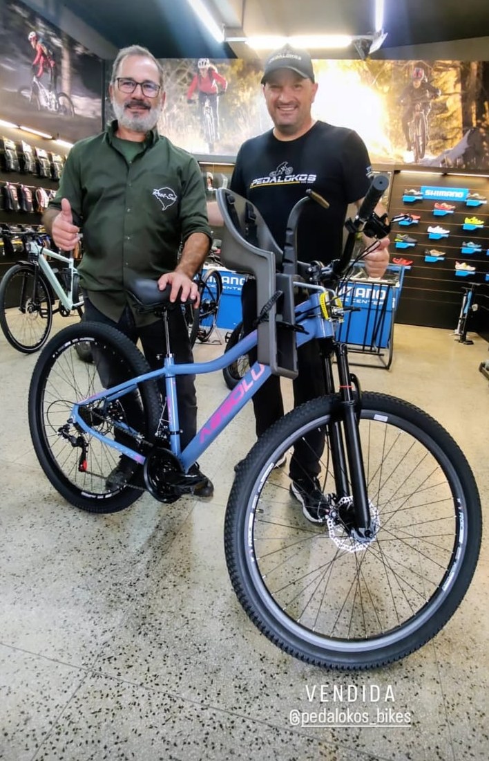 Cliente levando mountain bike laranja e acessórios comprados na loja