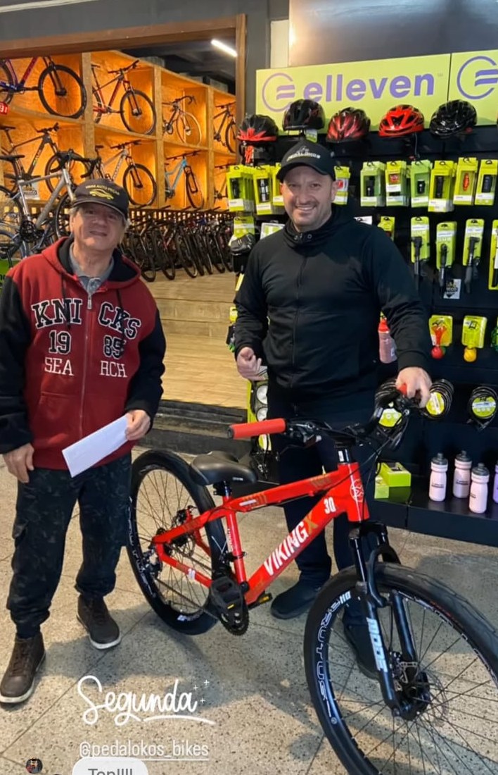 Cliente com mountain bike vermelha ao lado do painel de capacetes da loja
