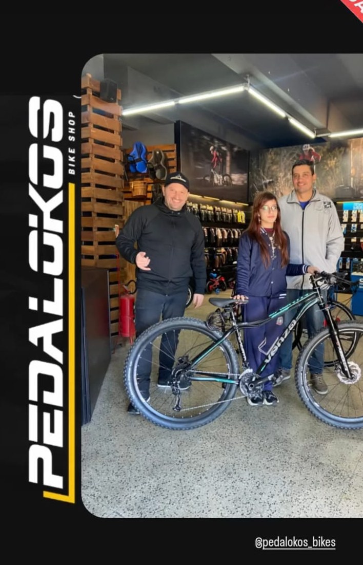 Dois clientes retirando mountain bike preta e azul na loja de bicicletas